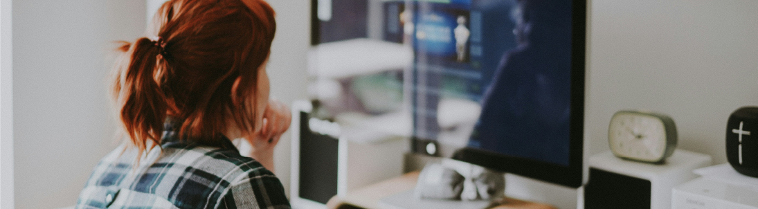 Woman with red hair wearing a flannel shirt views a website page on her desktop computer.